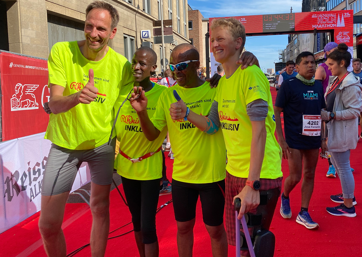 Extremsportlerin Tina Deeken, mit dem blinden Paralympioniker Henry Wanyoike und seinem Guide sowie Thomas Abel, Professor der Sporthochschule Köln von rechts gesehen im Ziel, Arm in Arm halten den Daumen nach oben.