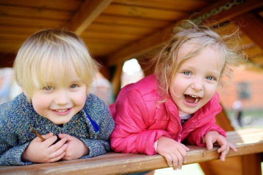 Zwei Kinder lehen über einem Holzgeländer und lachen.