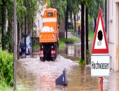 Foto: Bild einer Überschwemmungssituation mit einem Baufahrzeug und einem Schild.