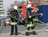 Feuerwehrmänner halten zwei Schläuche und tragen Feuerwehrkleidung.