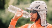 Bild eines Mannes, der Sonnenschutz und eine Sonnenbrille trägt und aus einer Wasserflasche trinkt.