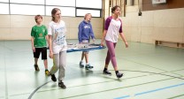 Kinder in der Sporthalle tragen ein Sportgerät.