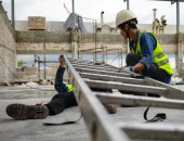 Bild: Ein Bauarbeiter hilft einem Kollegen der unter einer Leiter liegt