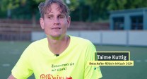 Standbild des Videos zeigt Taime Kuttig. Junger Mann mit kurzen Haaren, schlankes, kantiges Gesicht im Rhein-Inklusiv-Shirt auf einem Sportplatz.